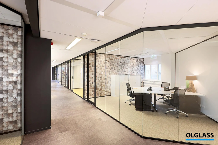 Jasne biuro typu open space z przeszklonymi gabinetami i szklanymi drzwiami po prawej stronie.