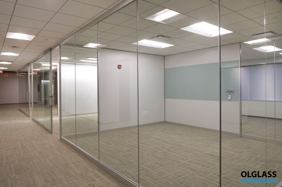 Przeszklony korytarz biurowy z wysokimi ściankami szklanymi i drzwiami w zabudowie.